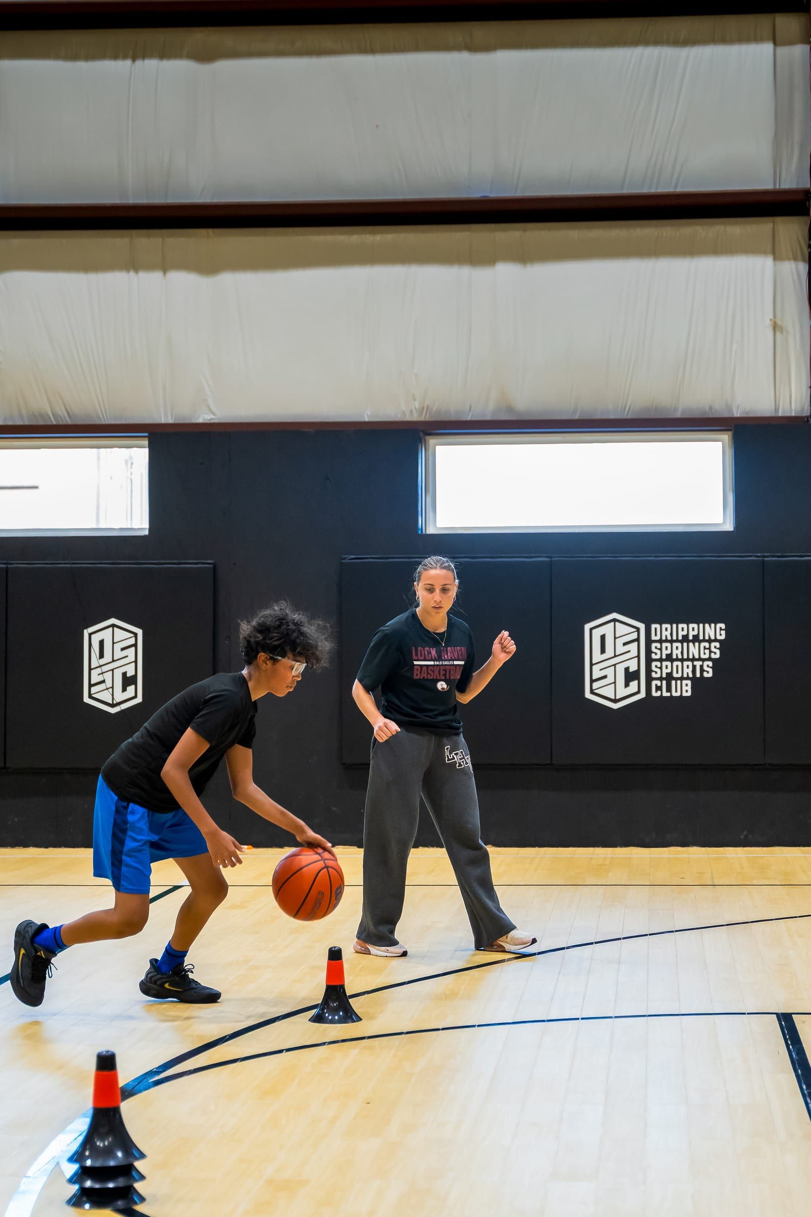 A player dribbling through cones under a coach's eye