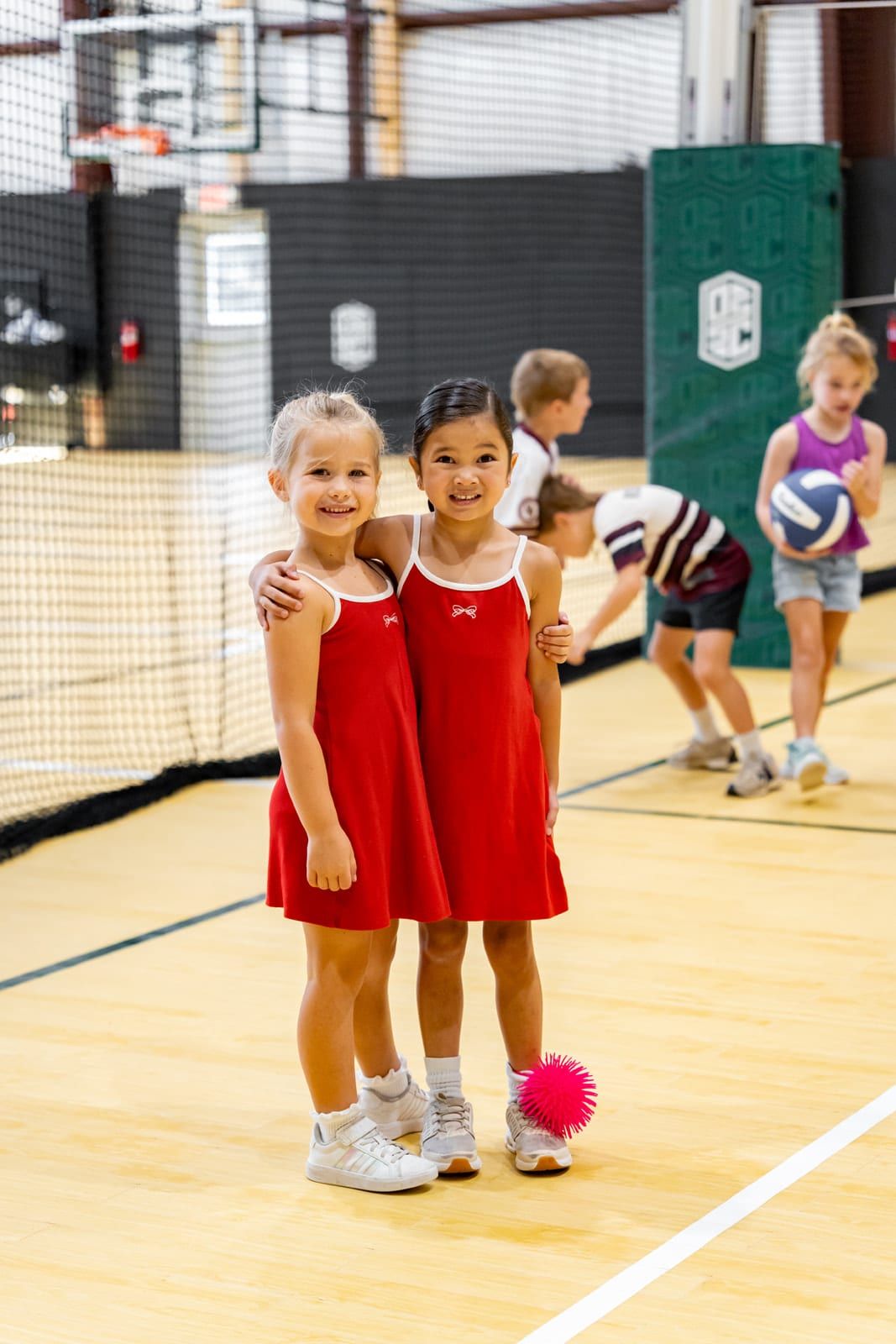 Two campers in red dresses arm in arm on the court