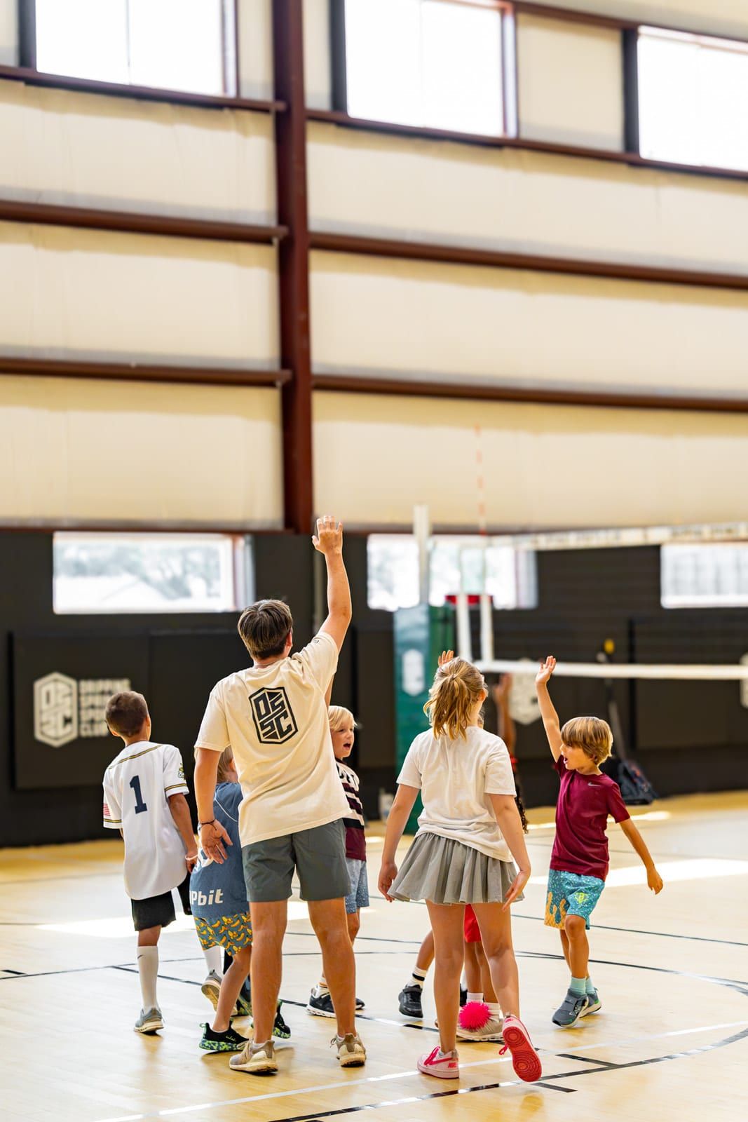 Five kids leap for a rebound under the basket while a coach watches from the baseline